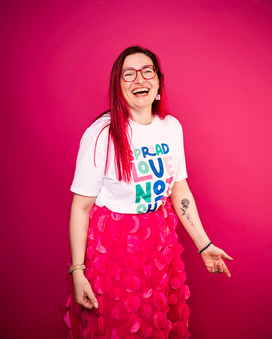 Person with red hair and colourful text spread love not shit shirt against a pink background photo by Haydn brown