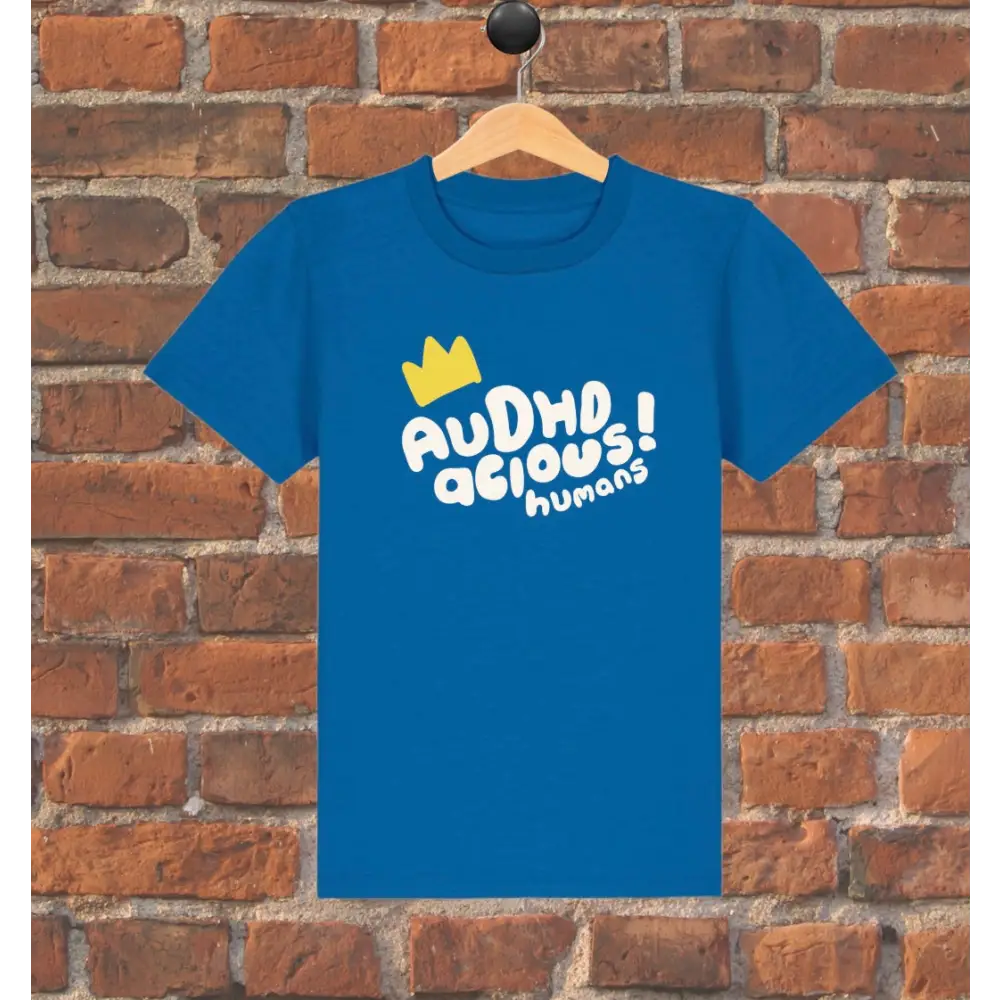 Blue t-shirt with white text and yellow crown graphic on a wooden hanger against a brick wall.