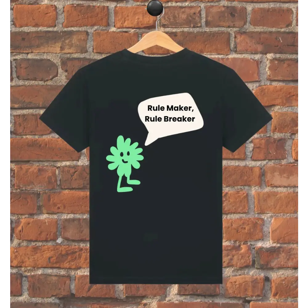Black t-shirt with green character and text 'Rule Maker, Rule Breaker' on a wooden hanger against a brick wall.