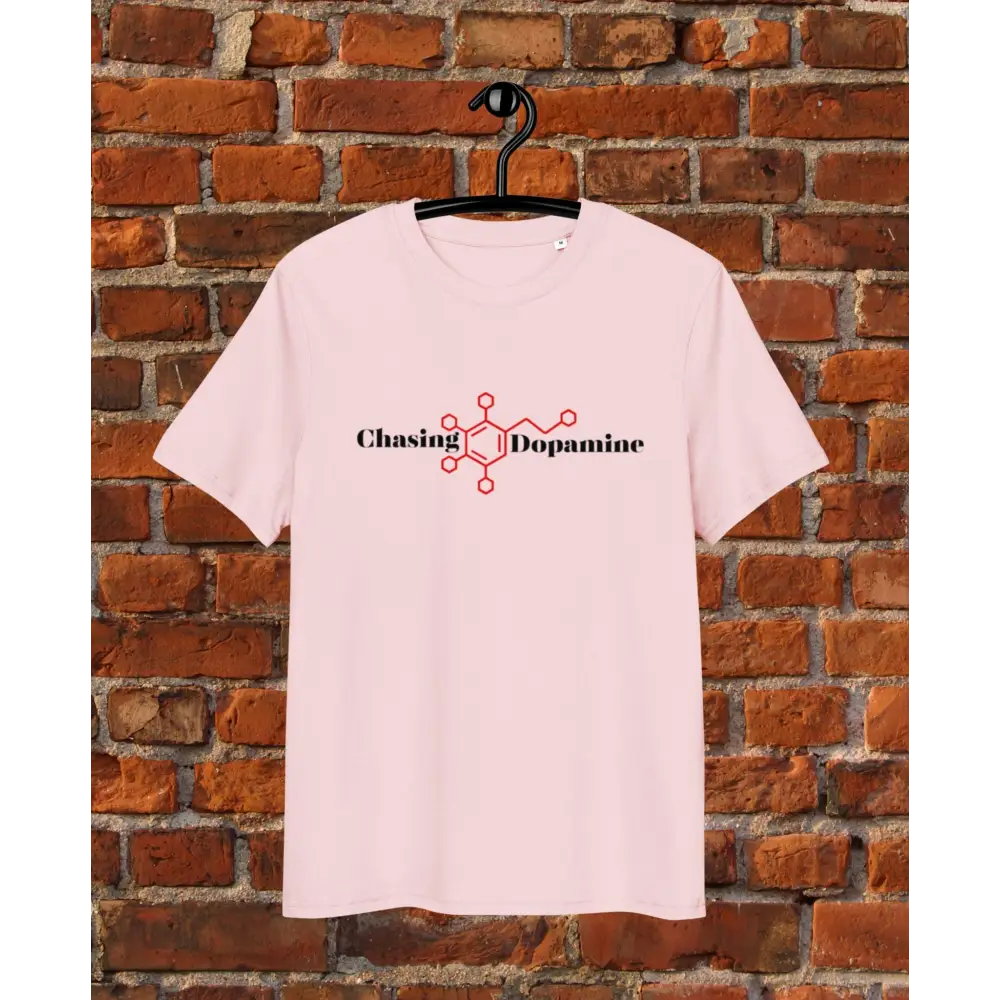 Pink t-shirt with 'Chasing Dopamine' design on a hanger against a brick wall.