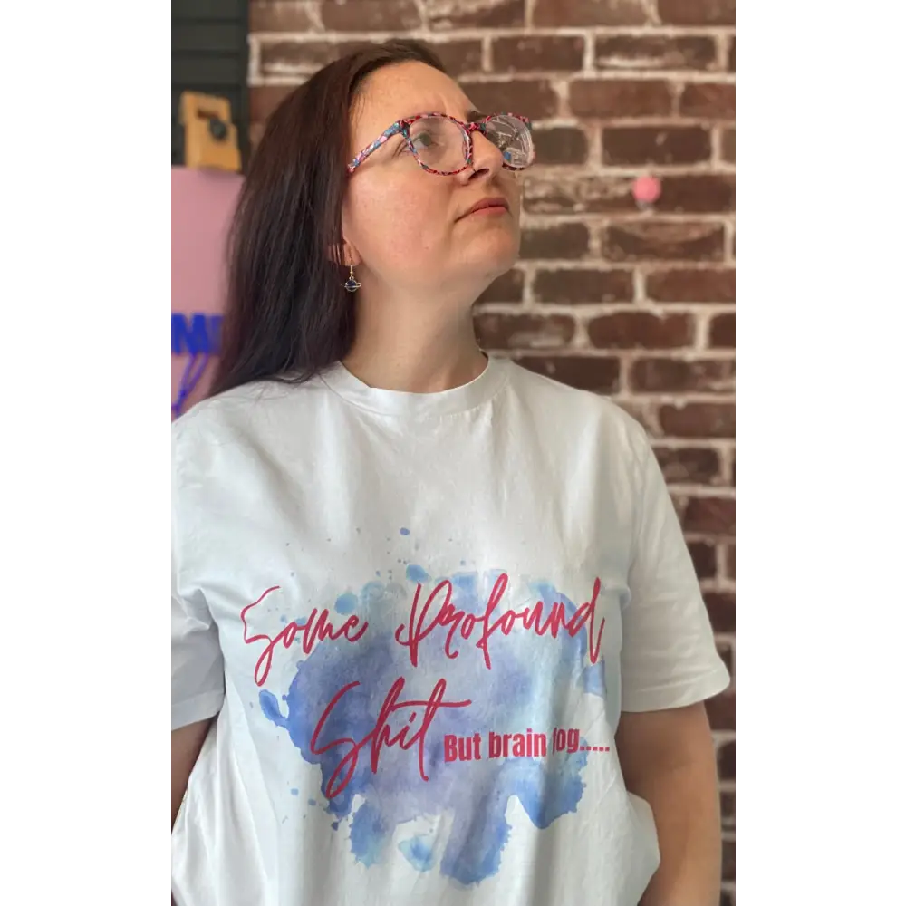 Person wearing a white t-shirt with colorful text and watercolor design against a brick wall.