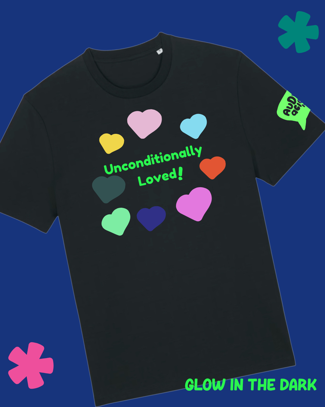 A black short-sleeve t-shirt with a colorful graphic of hearts and the text 'Unconditionally Loved!' on the front, plus a green speech bubble on the sleeve that reads 'GLOW IN THE DARK'. The t-shirt is displayed on a dark blue background with decorative pink and green flower shapes.