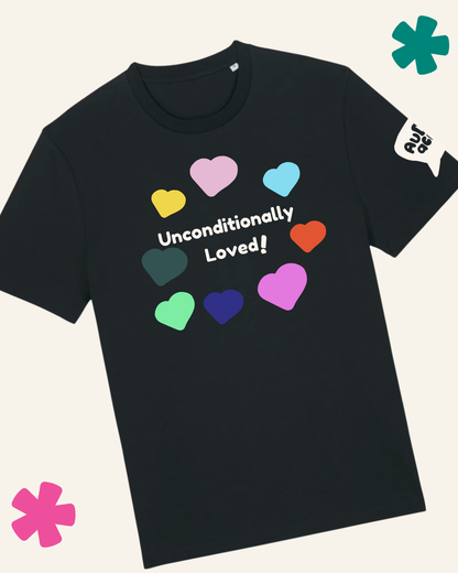 A black short-sleeve t-shirt with a colorful heart graphic and the text 'Unconditionally Loved!' printed on the chest. The shirt is displayed on a light cream background with decorative colorful flower graphics in the corners and a speech bubble graphic on the sleeve.
