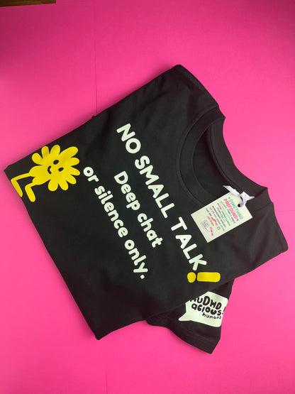 A black t-shirt laid flat on a bright pink background, featuring a yellow cartoon sun character and the text 'NO SMALL TALK Deep chat or silence only.' in white, along with a hangtag and a small 'ROUND GEEKS' sticker.