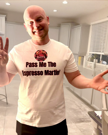 A Dave man in a kitchen wearing a white graphic t-shirt with the text 'Pass Me The Espresso Martin' and a circular 'SLOTS' logo, gesturing with his hands.