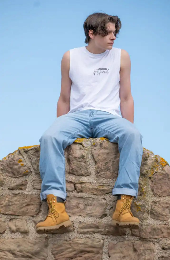 Person sitting on a stone powder house in Seahouses wearing a white sleeveless shirt, light blue jeans, and yellow boots against a clear blue sky.