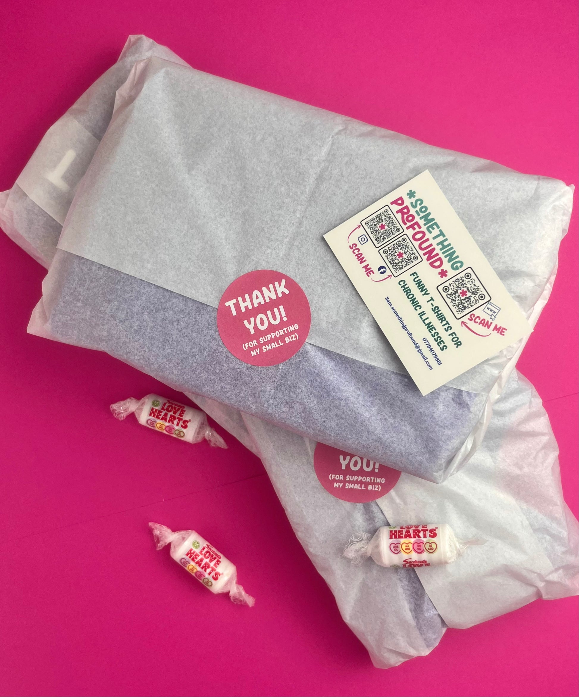 A gift-wrapped package wrapped in translucent tissue paper with a round pink 'Thank You!' sticker and a white something profound business card. three small wrapped love heart sweets are placed on a bright pink background.