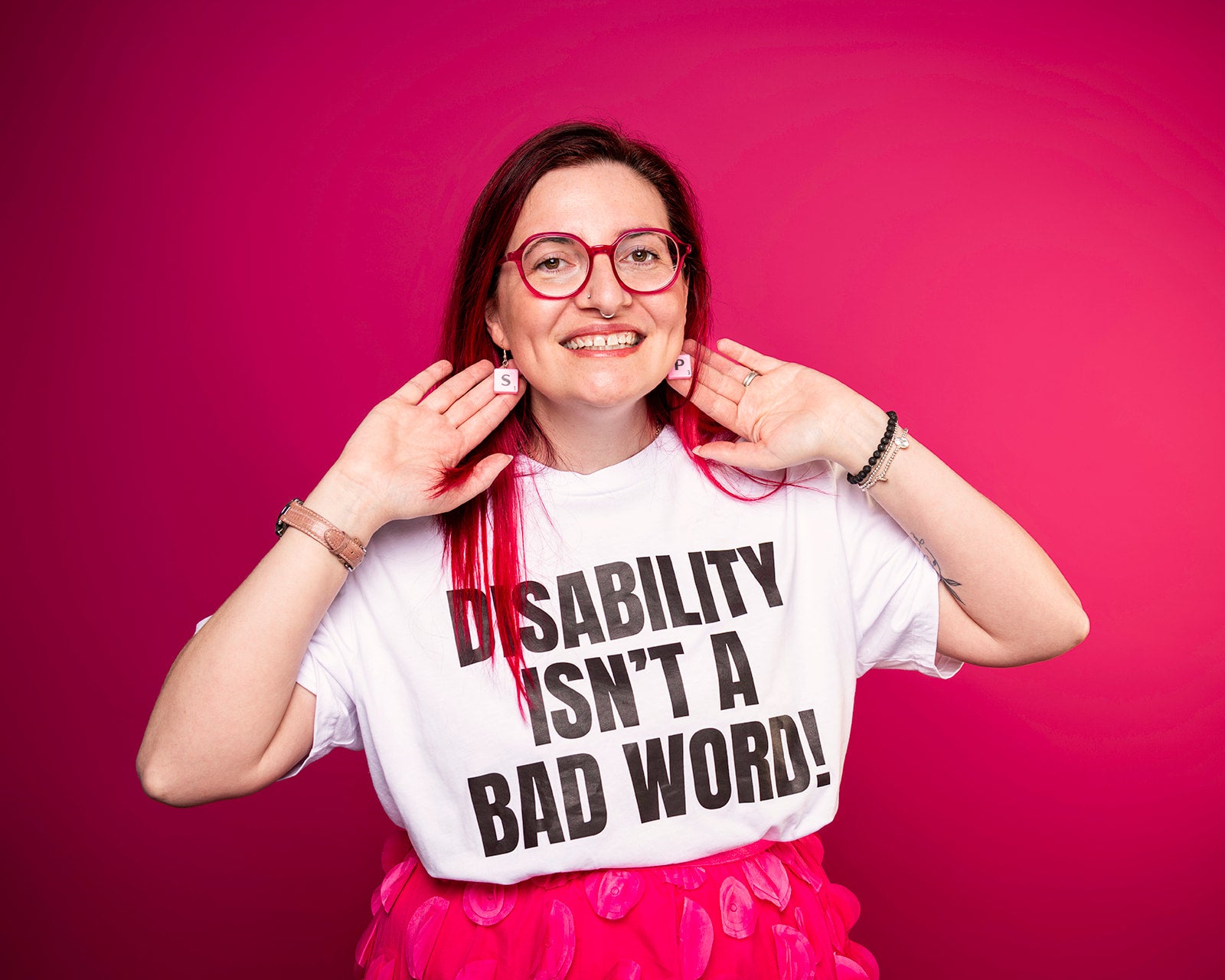 Sam wearing a t-shirt with 'Disability Isn't a Bad Word!' on a pink background photo by Haydn brown