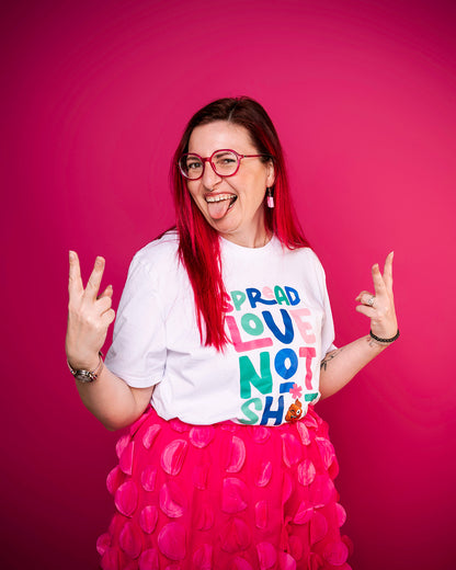 Person with red hair and glasses wearing a white t-shirt with colourful text spread love not shit on a pink background