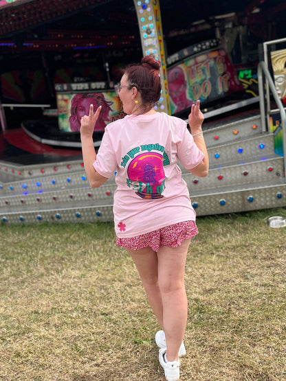 Sam in pink take your negative energy and fk off shirt and shorts standing in front of a colorful waltzer at slaters funfair 