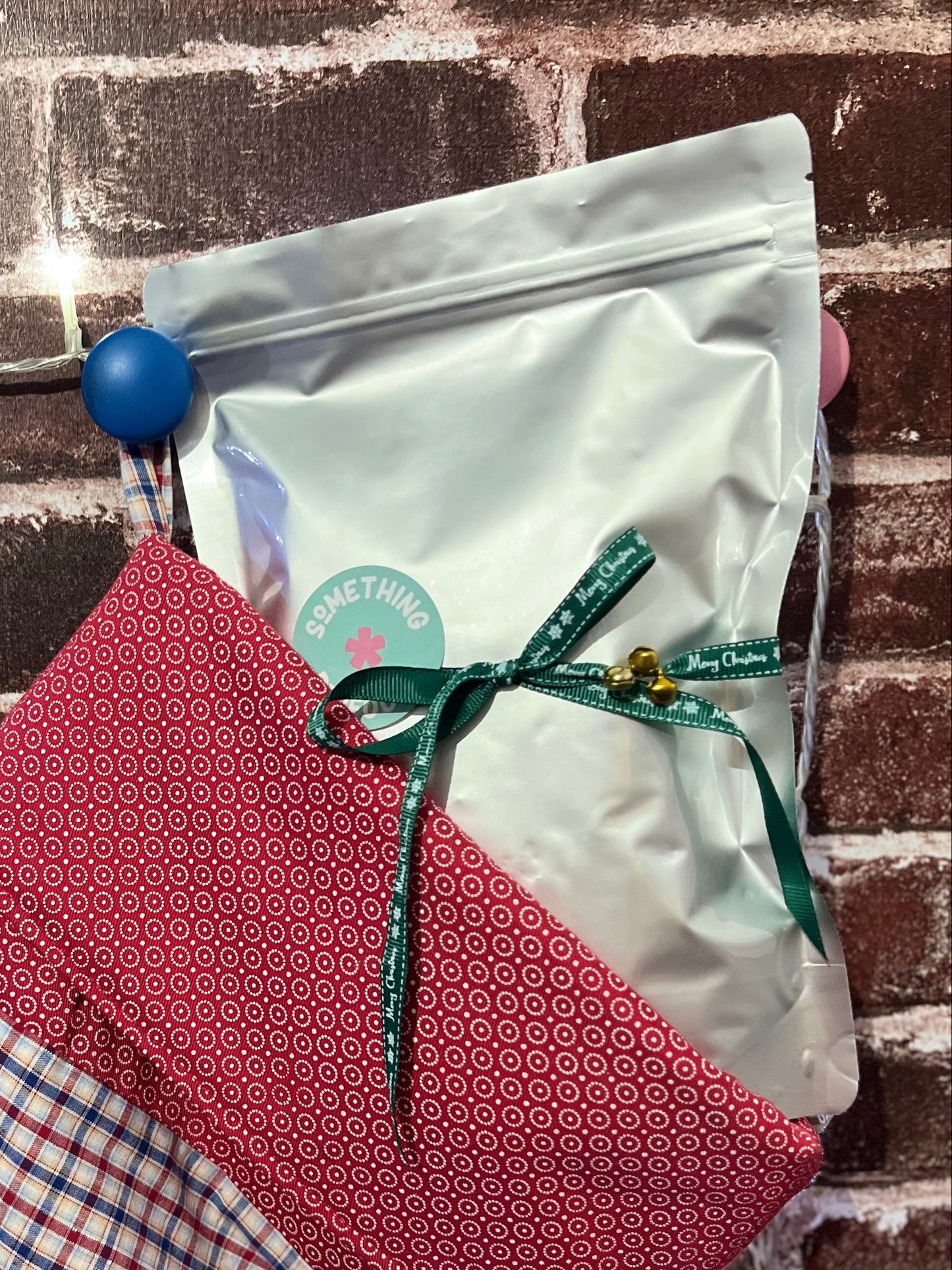 Red and blue checkered stocking with a white bag tied with a green ribbon against a brick wall.