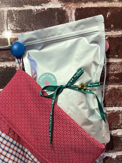 Red and blue checkered stocking with a white bag tied with a green ribbon against a brick wall.