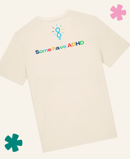 A natural raw short-sleeve t-shirt shown from the back, featuring a colorful graphic with a lightbulb containing the number 8 and the text 'Some have ADHD' in rainbow colors. The t-shirt is displayed on a light cream background with decorative pink and teal flower graphics in the corners. Unite Club x Something Profound