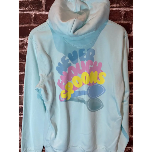 Light blue hoodie with colorful text and spoon graphic against a brick wall background