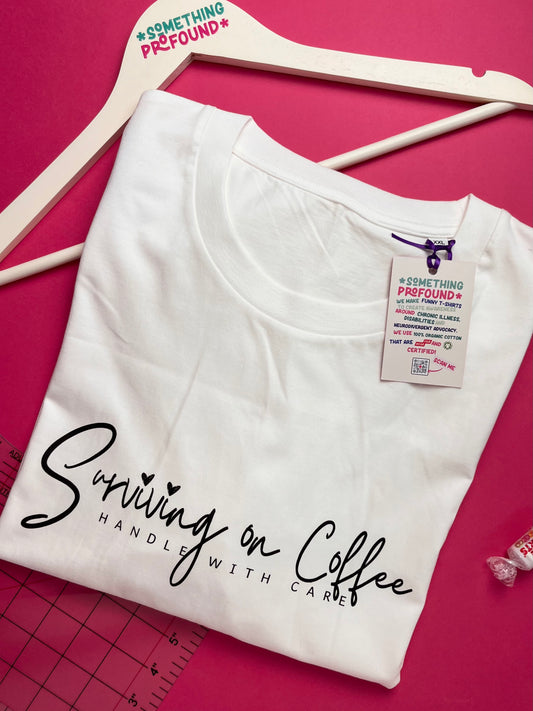 White t-shirt with 'Surviving on Coffee Handle with Care' text on a pink background