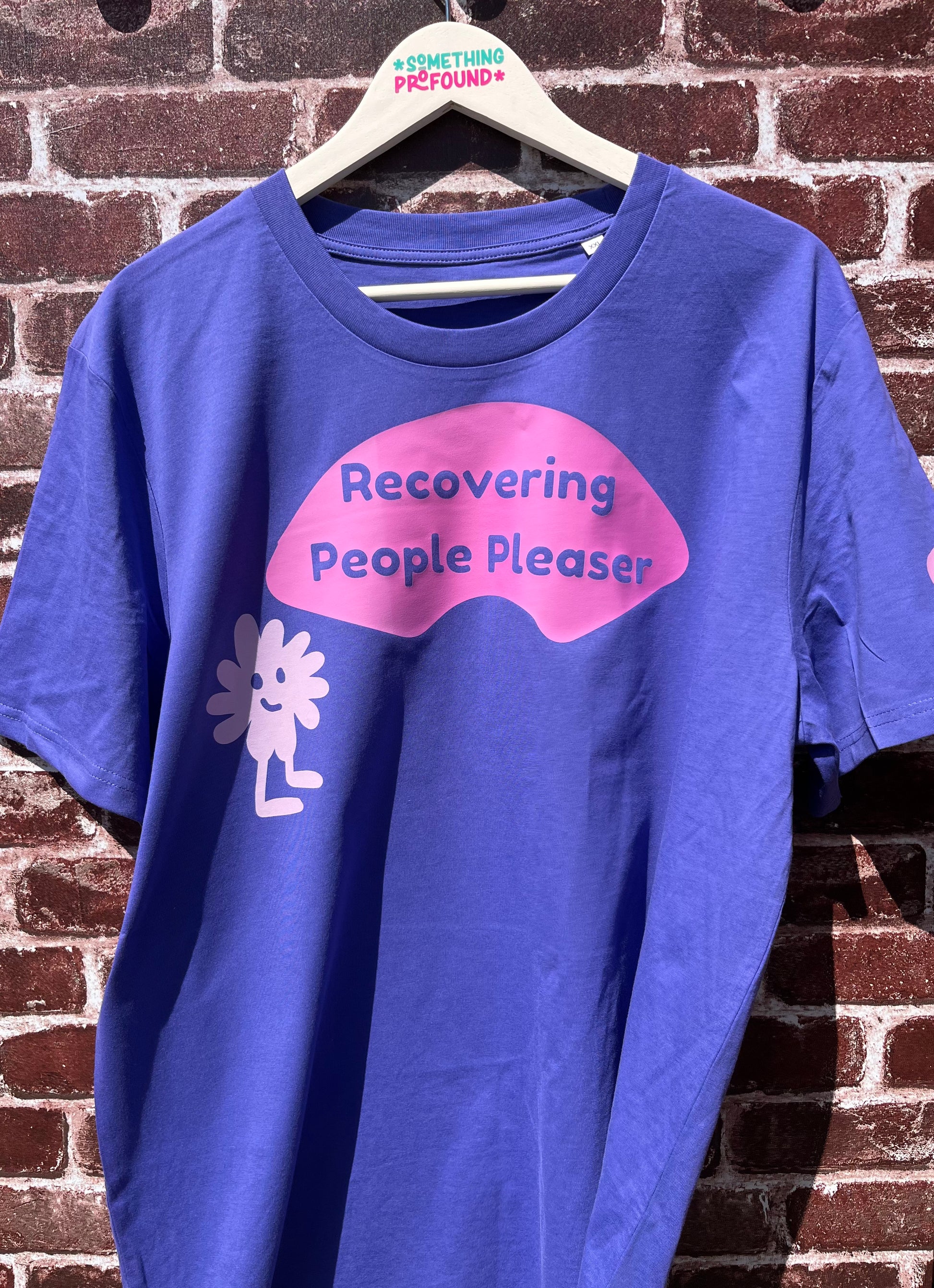 Blue t-shirt with pink and white graphic design on a hanger against a brick wall.