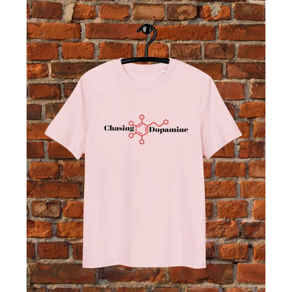 Pink t-shirt with 'Chasing Dopamine' design on a hanger against a brick wall.