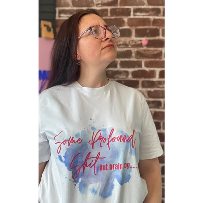 Person wearing a white t-shirt with colorful text and watercolor design against a brick wall.