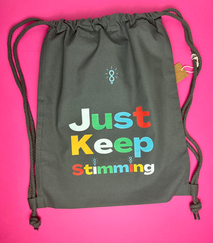 A dark gray drawstring bag with colorful text reading 'Just Keep Stimming' on a bright pink background.
