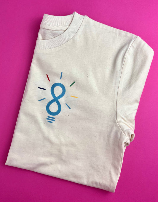 A folded off-white crewneck t-shirt with a blue and multicolor lightbulb graphic on the chest, displayed on a solid pink background.