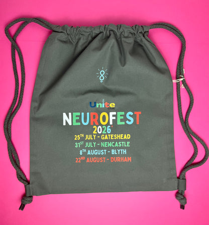 A dark gray drawstring backpack with 'Unite NeuroFest 2026' printed on the front, laid flat on a bright pink background.
