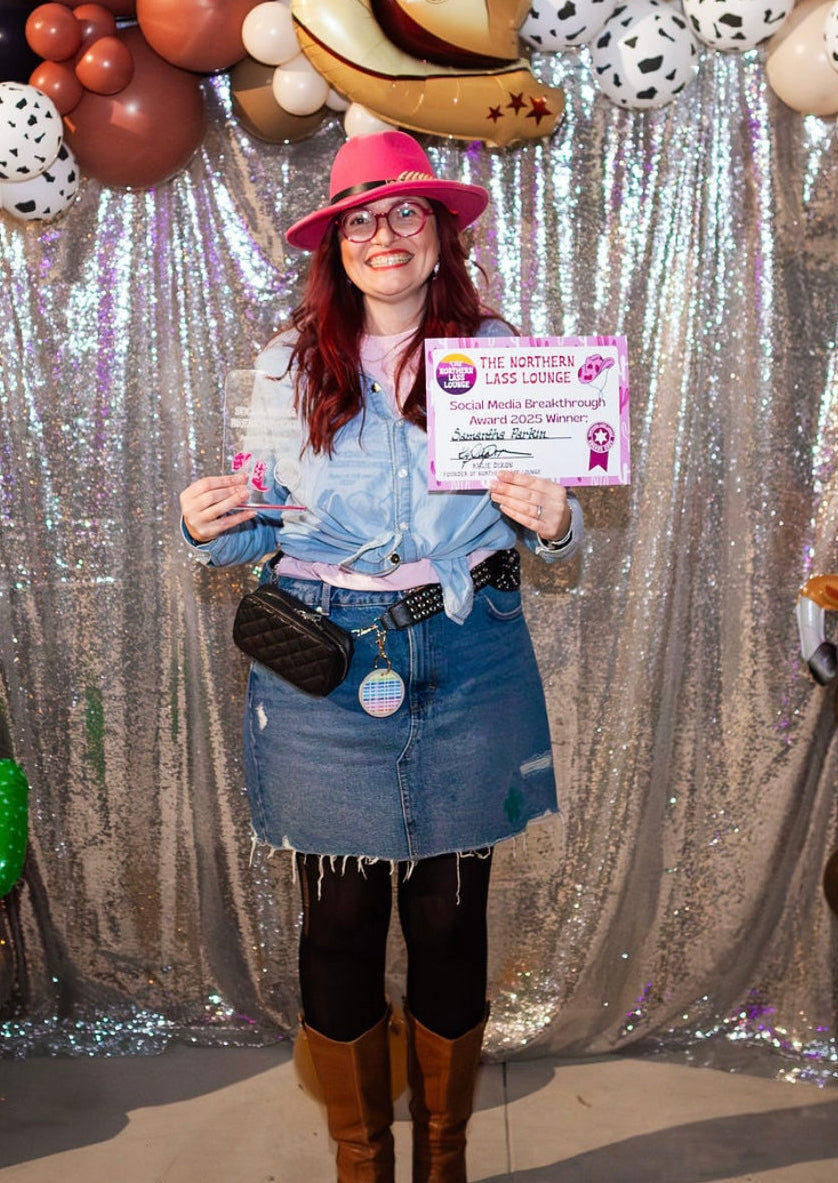 Person holding a certificate in front of a festive backdrop with balloons and decorations winner_sam Norhern lass lounge social media breakthrough